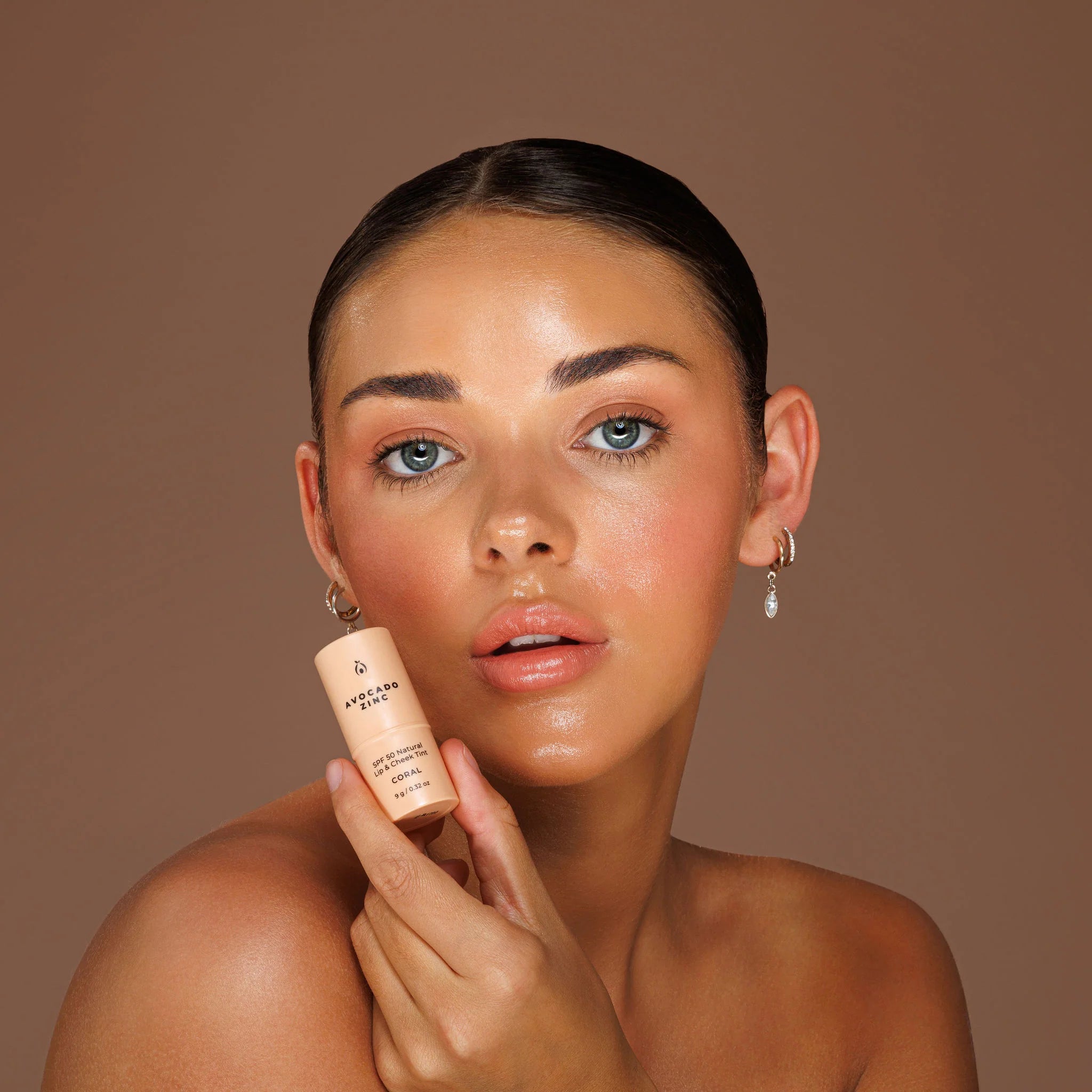 Woman holding a skincare product against a brown background for avocado zine lip tint and cheek tint